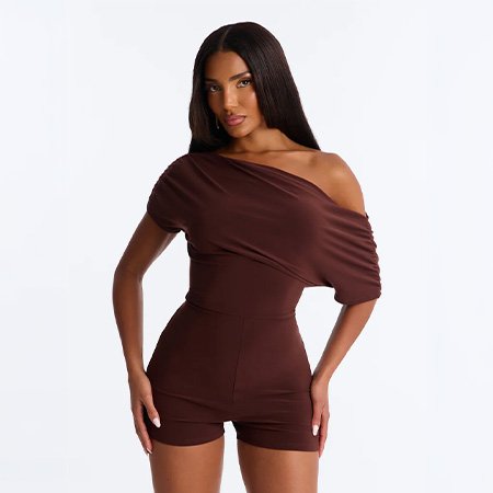 Woman posing in a chocolate brown off-the-shoulder romper, showcasing chic women's summer fashion against a white studio background.