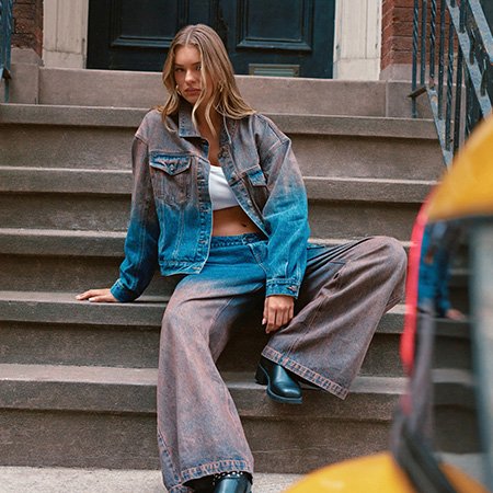 Woman posing on urban steps in a trendy blue and brown gradient denim jacket and matching wide-leg jeans for a new fall streetwear collection.