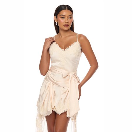 Model in an elegant champagne satin mini dress with lace trim and waist tie, showcasing a chic cocktail party look on a white background.