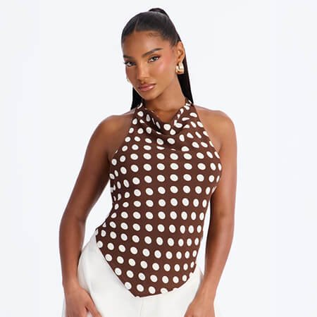 Woman poses in a chic brown and white polka dot halter neck top paired with white trousers, showcasing the new summer fashion collection.